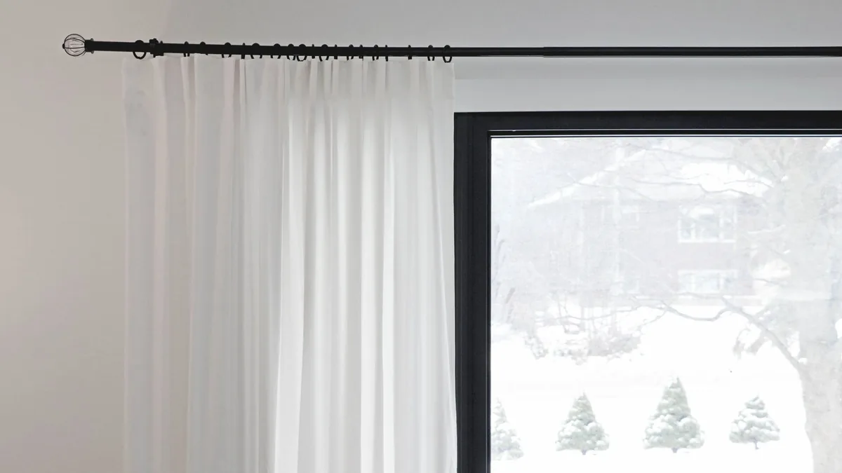 Cortinas blancas cubriendo parcialmente una ventana tras la que se ve un paisaje nevado.