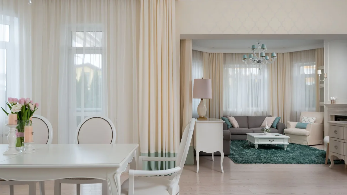 Salón y comedor de planta abierta con la ventana vestida al fondo y mobiliario claro.