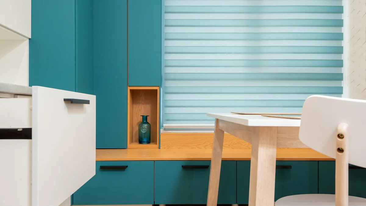 Estor de bandas horizontales bajado sobre la ventana de una cocina moderna, con la luz del exterior atravesando el tejido.