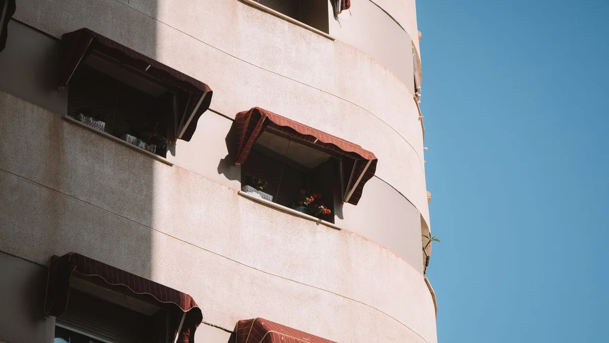 Fachada de un edificio de viviendas en Málaga con toldos desplegados en los balcones, a pleno sol.