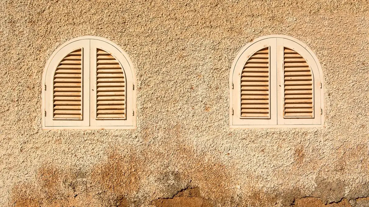 Fachada con dos ventanas en arco cerradas con contraventanas de lamas, vistas desde el exterior.